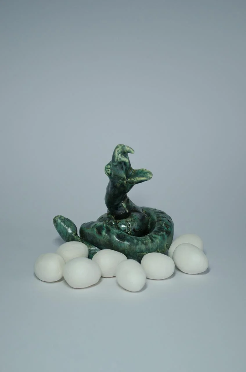 Escultura verde de una serpiente enroscada rodeada de formas blancas.